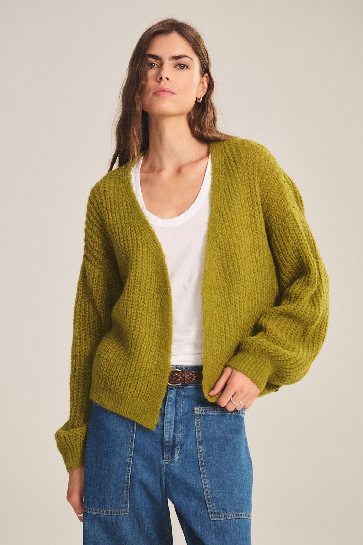 A person wears the Velvet by Graham & Spencer RANYA ALPACA CARDIGAN in olive-green over a white tee and blue jeans, standing against a neutral background to showcase cozy layering.
