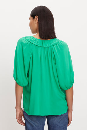 The woman is seen from the back, wearing a green blouse with a v-neckline, the ALEGRA V-NECK TOP by Velvet by Graham & Spencer.