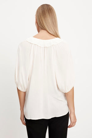 The woman is seen from behind in a white Velvet by Graham & Spencer ALEGRA V-NECK TOP with puff sleeves.