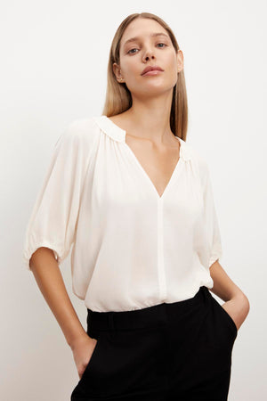 The model is wearing a cream ALEGRA V-NECK TOP with puff sleeves and black pants. (Brand Name: Velvet by Graham & Spencer)