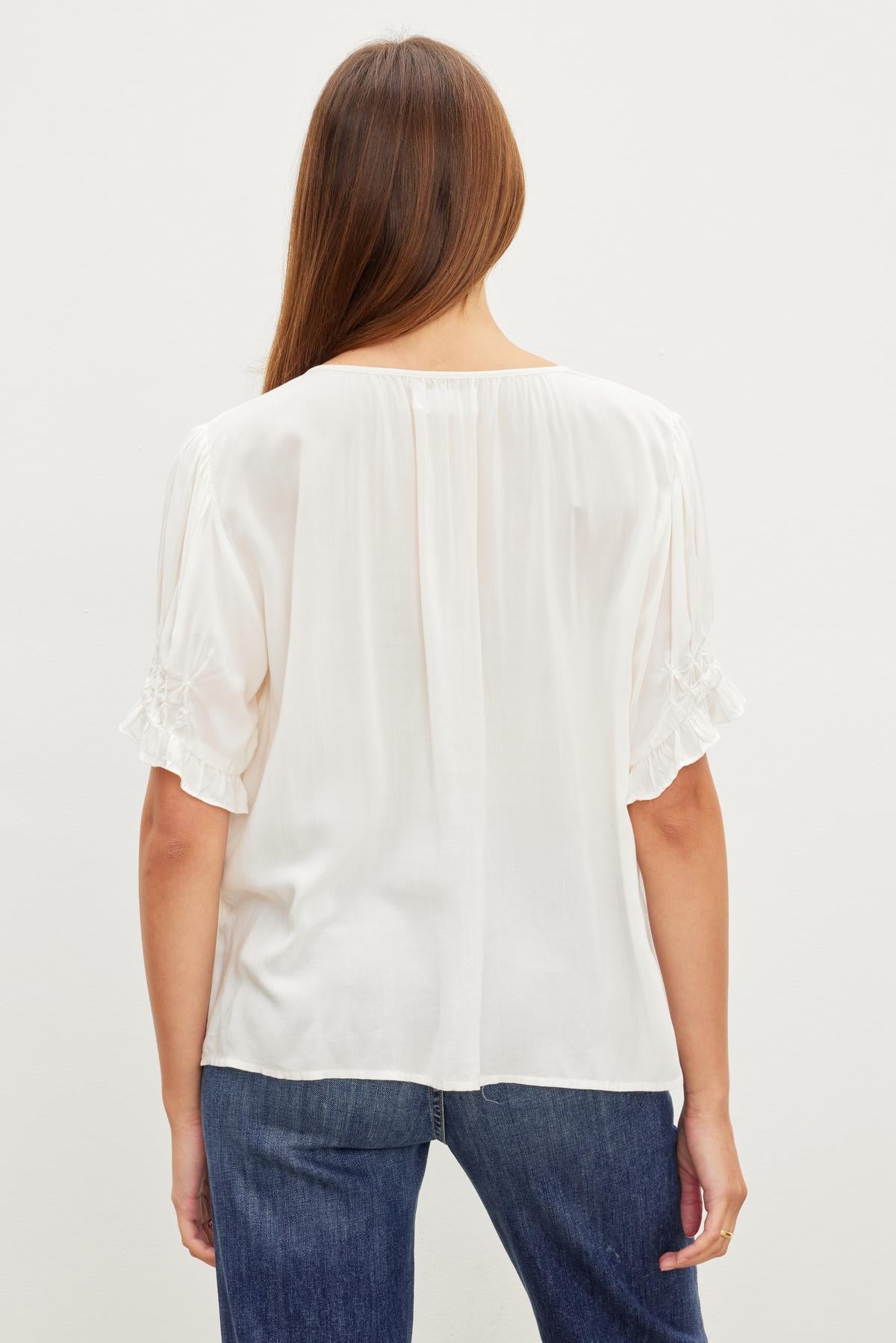 A woman with long hair is facing away, wearing a CALISSA BLOUSE by Velvet by Graham & Spencer and blue jeans.-37162878730433