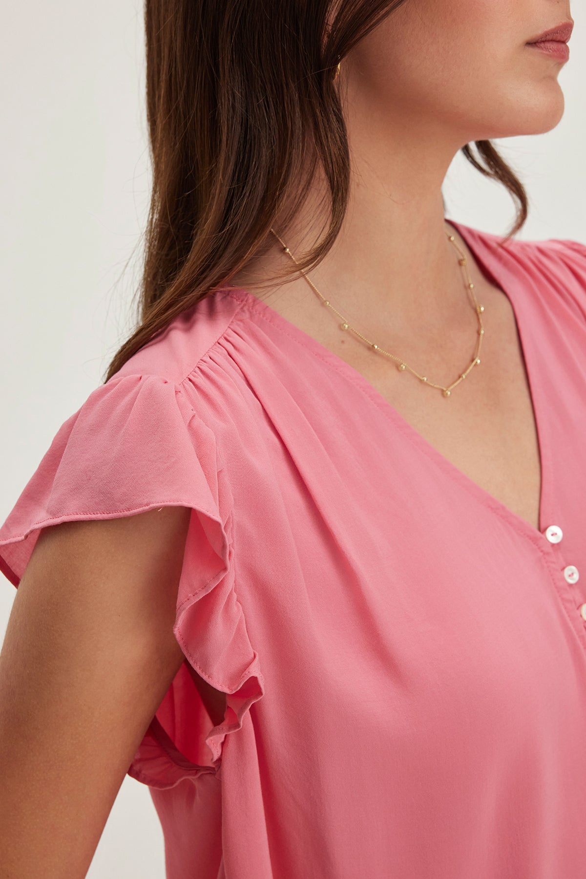 A woman wearing the Velvet by Graham & Spencer MALTA TOP, a pink blouse with flutter sleeves, a flattering v-neckline, and accessorized with a delicate gold necklace.