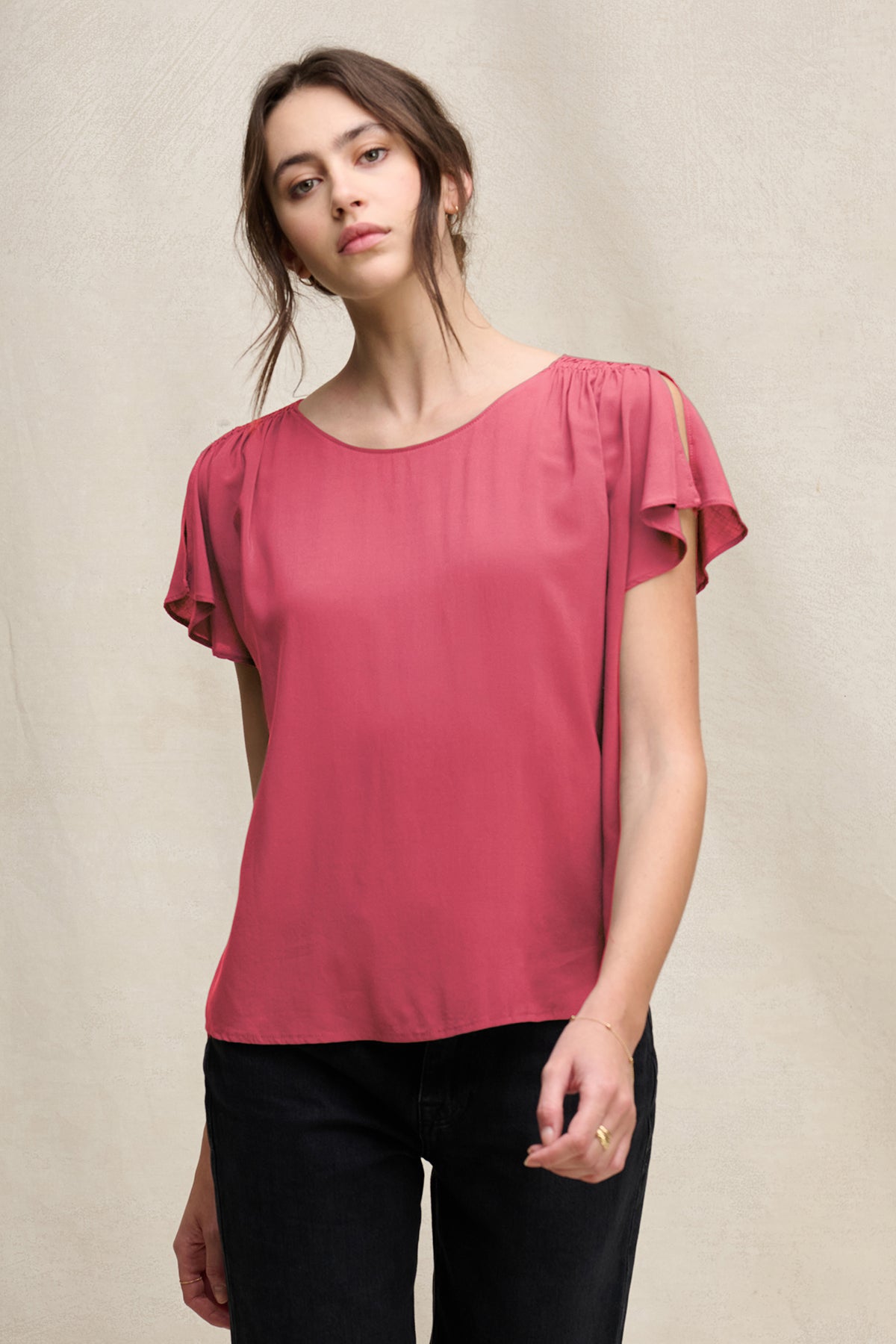 A person wears the MARCEL TOP by Velvet by Graham & Spencer, a rose-colored short-sleeve rayon challis blouse with smocked shoulders, paired with black pants, against a neutral background.