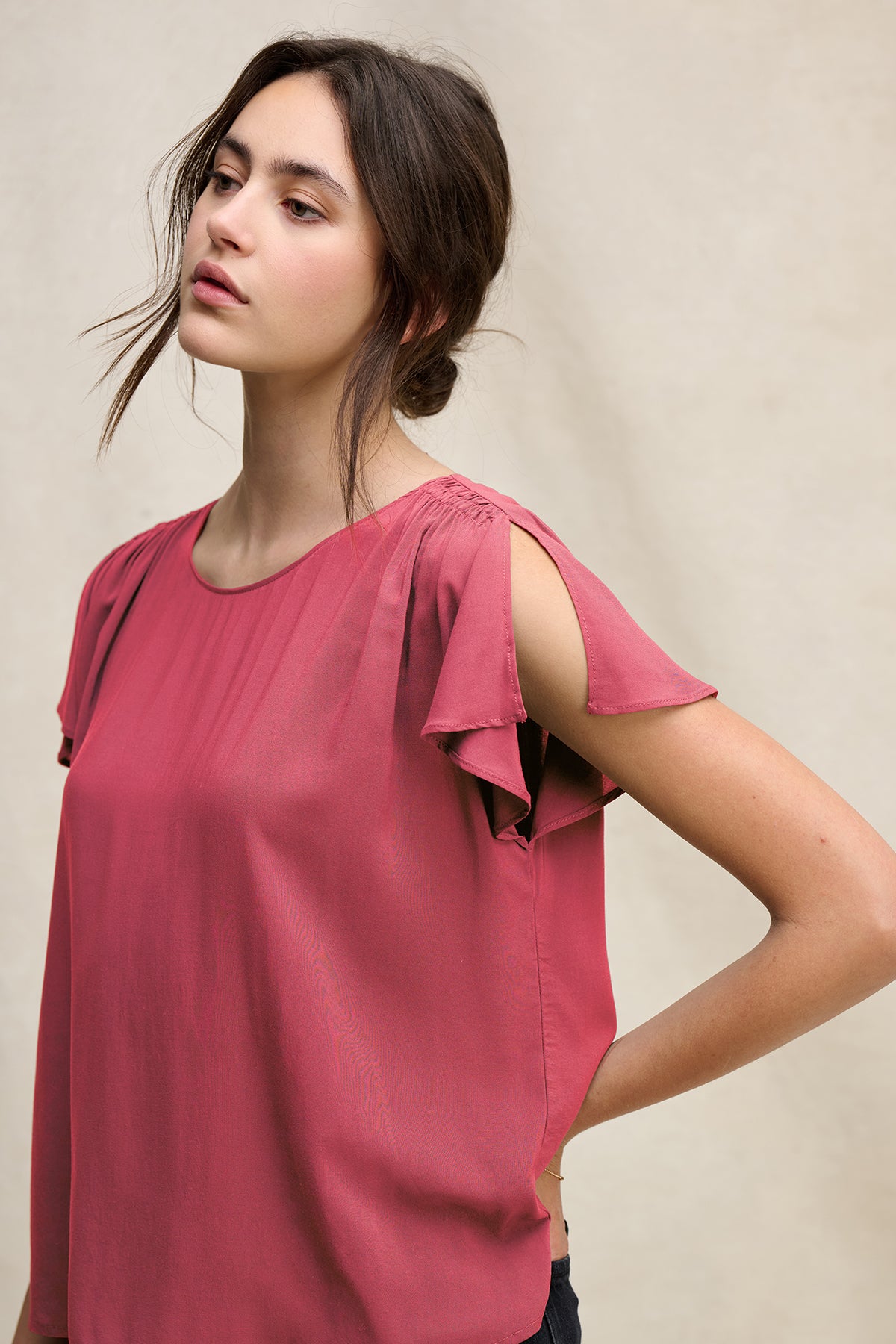 A woman with long brown hair in a loose bun wears the MARCEL TOP by Velvet by Graham & Spencer, a rose-colored rayon challis blouse with split shoulder details and a keyhole closure, standing against a neutral background.