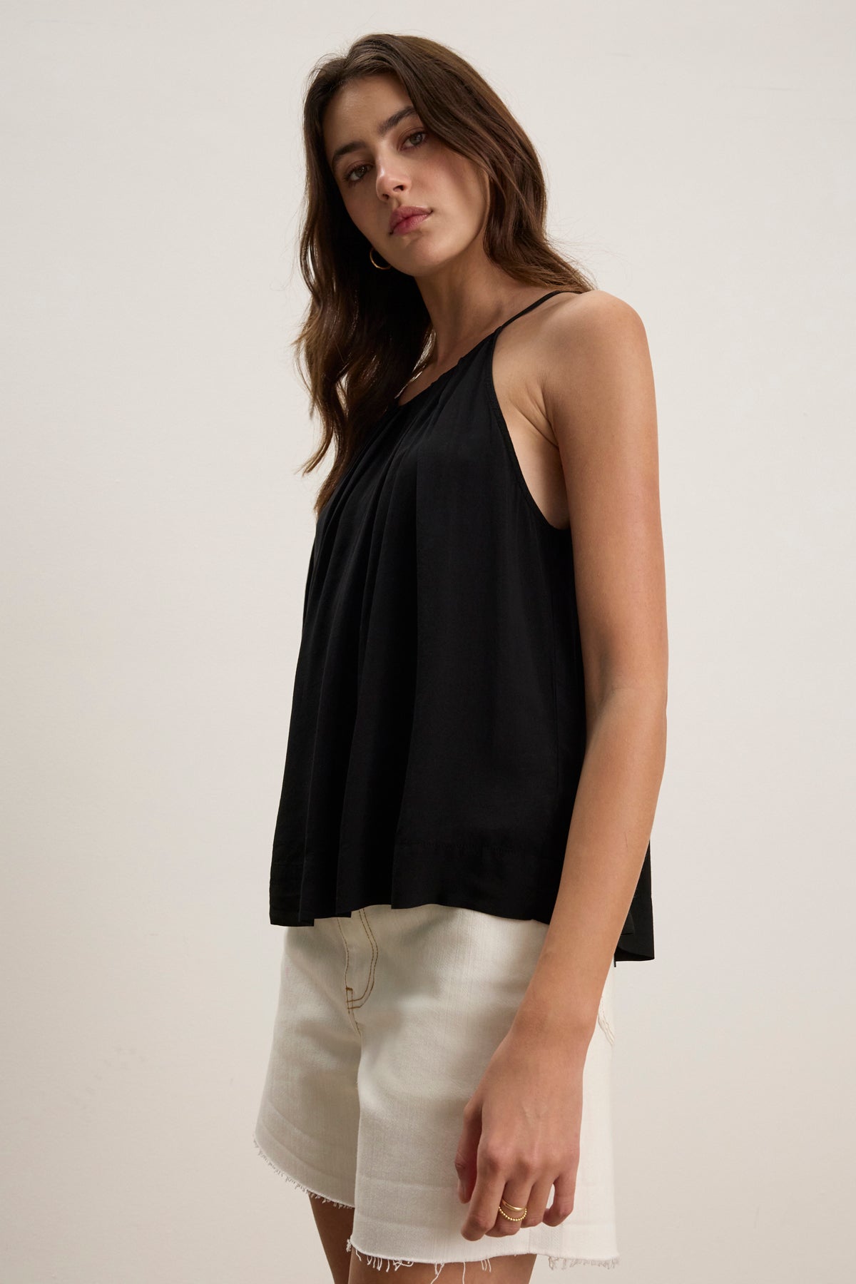 A person wearing the PIPER TANK TOP by Velvet by Graham & Spencer in pleated fabric and light-colored shorts stands against a plain off-white background.