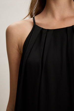 A close-up of a person wearing the PIPER TANK TOP by Velvet by Graham & Spencer, a sleeveless black pleated fabric top with thin straps, shown from shoulders to upper chest.