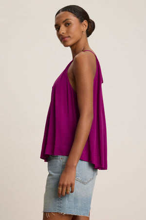 A woman in profile wears the Velvet by Graham & Spencer PIPER TANK TOP, a loose-fitting, sleeveless, high neck magenta top in Rayon Challis, paired with a light blue denim skirt against a plain background.