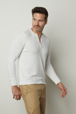 A man wearing a Velvet by Graham & Spencer Anderson Rib Knit Henley shirt and tan pants.