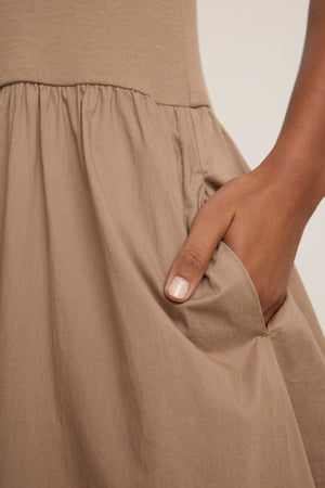 A person with medium brown skin places their right hand in the pocket of the taupe AMELIA DRESS by Velvet by Graham & Spencer, made from versatile cotton poplin.