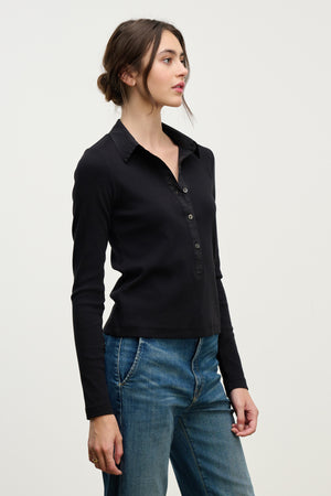 A woman stands in profile against a light background, wearing the ARVINE SHIRT by Velvet by Graham & Spencer—a black, fitted cotton poplin collared shirt with buttons—paired with blue jeans.