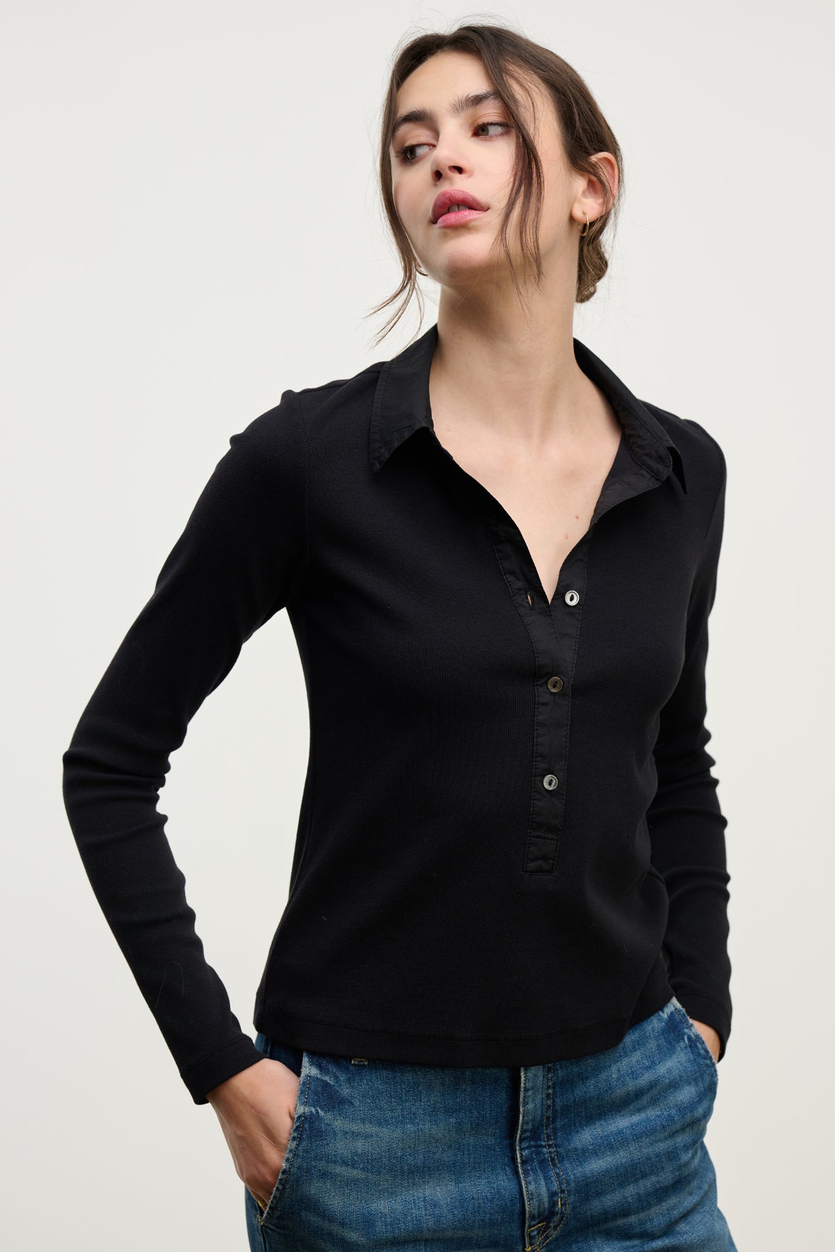 A woman wears the ARVINE SHIRT by Velvet by Graham & Spencer—a black long-sleeve ribbed shirt with a cotton poplin collar—paired with blue jeans, standing against a plain light background.-39800284348609