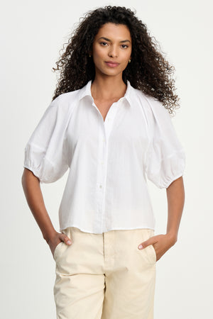 A woman models the AUTUMN SHIRT by Velvet by Graham & Spencer—a white cotton poplin, short-sleeve top—paired with light beige pants, exuding effortless everyday style against a plain background.