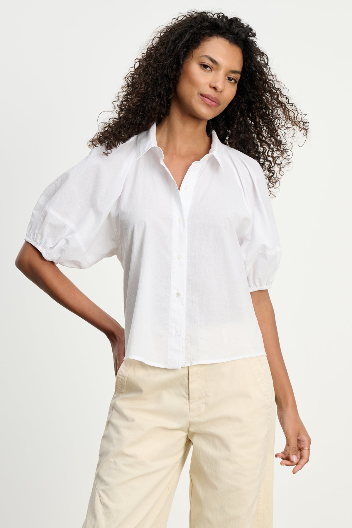 A woman wears the AUTUMN SHIRT by Velvet by Graham & Spencer—a cotton poplin top with puff sleeves—paired with light beige pants, standing against a plain background for an effortlessly chic everyday look.