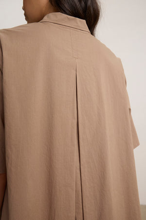 A person is shown from behind wearing the DRIANA DRESS by Velvet by Graham & Spencer, a light brown, short-sleeved dress featuring a back pleat detail and subtle side seam pockets.