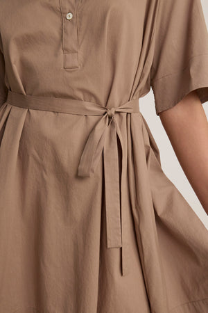 Close-up of the DRIANA DRESS by Velvet by Graham & Spencer, featuring taupe cotton poplin, a tied fabric belt at the waist, side seam pockets, and a partial button placket at the neckline.