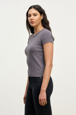 A woman with long dark hair, wearing the EDDIE TEE by Velvet by Graham & Spencer and black jeans, stands sideways against a plain light background.