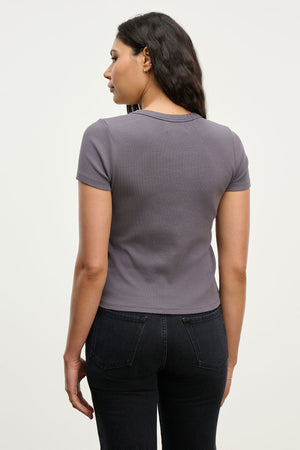 A woman stands with her back to the camera in the EDDIE TEE by Velvet by Graham & Spencer, a fitted cropped crew neck top, paired with black jeans against a plain light background.