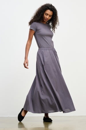 A woman models the FILLA SKIRT by Velvet by Graham & Spencer—a long, lightweight summer skirt with pockets and an elastic waist—paired with a short-sleeve, fitted gray top, standing against a plain white background.