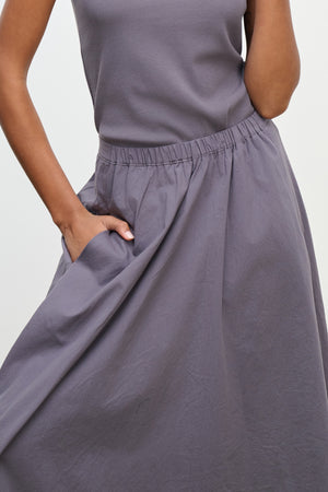 A person wearing the FILLA SKIRT by Velvet by Graham & Spencer—a lightweight, sleeveless gray top and matching skirt with an elastic waistband—stands with one hand in the skirt's pocket.