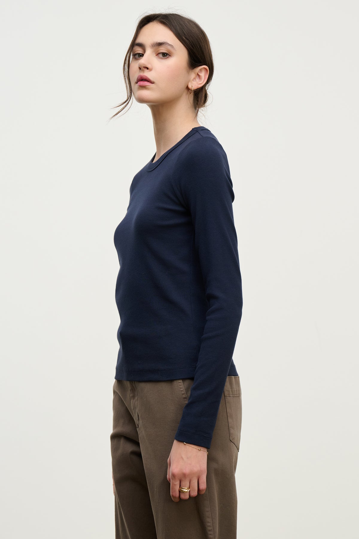 A person wears the LOTTA TEE by Velvet by Graham & Spencer, a long-sleeve ribbed cotton top, with brown pants while standing sideways against a plain light background.-39814898450625