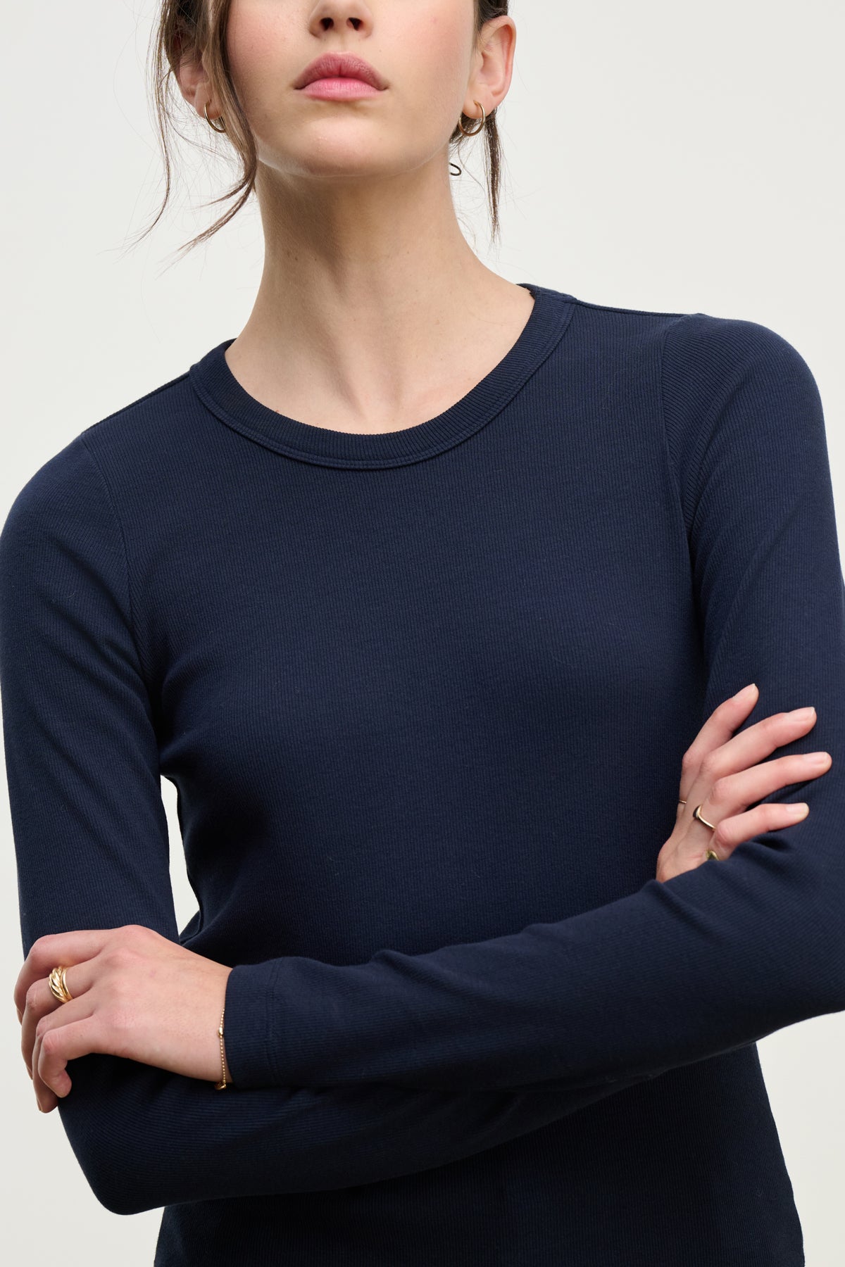 A person with long brown hair, arms crossed and shown from the shoulders down, is wearing the LOTTA TEE by Velvet by Graham & Spencer—a navy blue ribbed cotton long sleeve top.-39814898385089