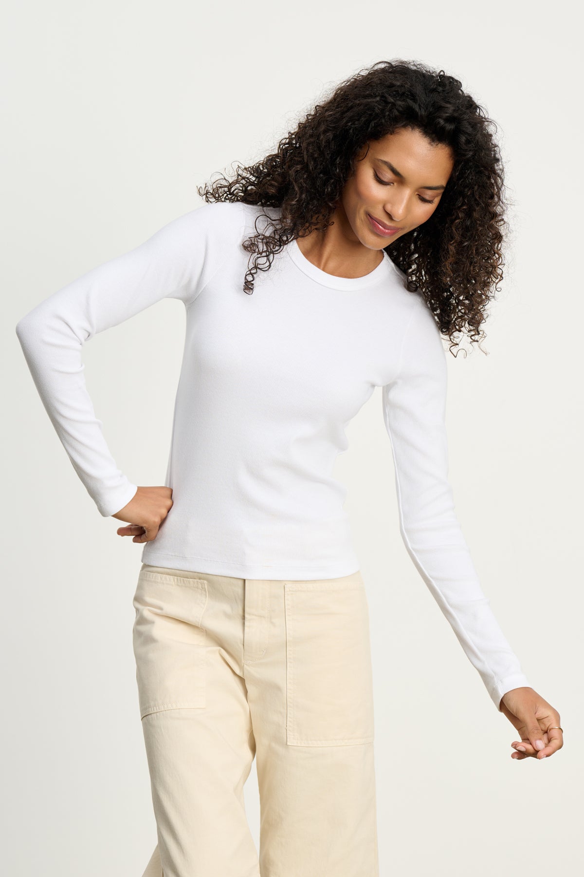 A person models the Velvet by Graham & Spencer LOTTA TEE in white ribbed cotton, paired with light beige pants, standing against a plain light background with one hand on their hip and the other relaxed.-39617521418433