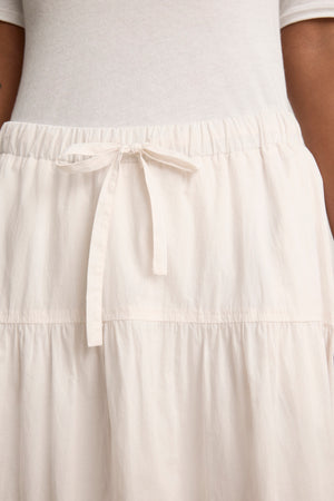 A close-up of a person wearing the LOUI SKIRT by Velvet by Graham & Spencer, a white or light beige elastic waist maxi skirt with a drawstring tie, paired with a matching top.