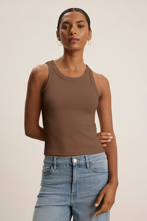 A woman wears the SARI TANK TOP by Velvet by Graham & Spencer in brown with light blue jeans against a plain background—a modern essential for effortless style.