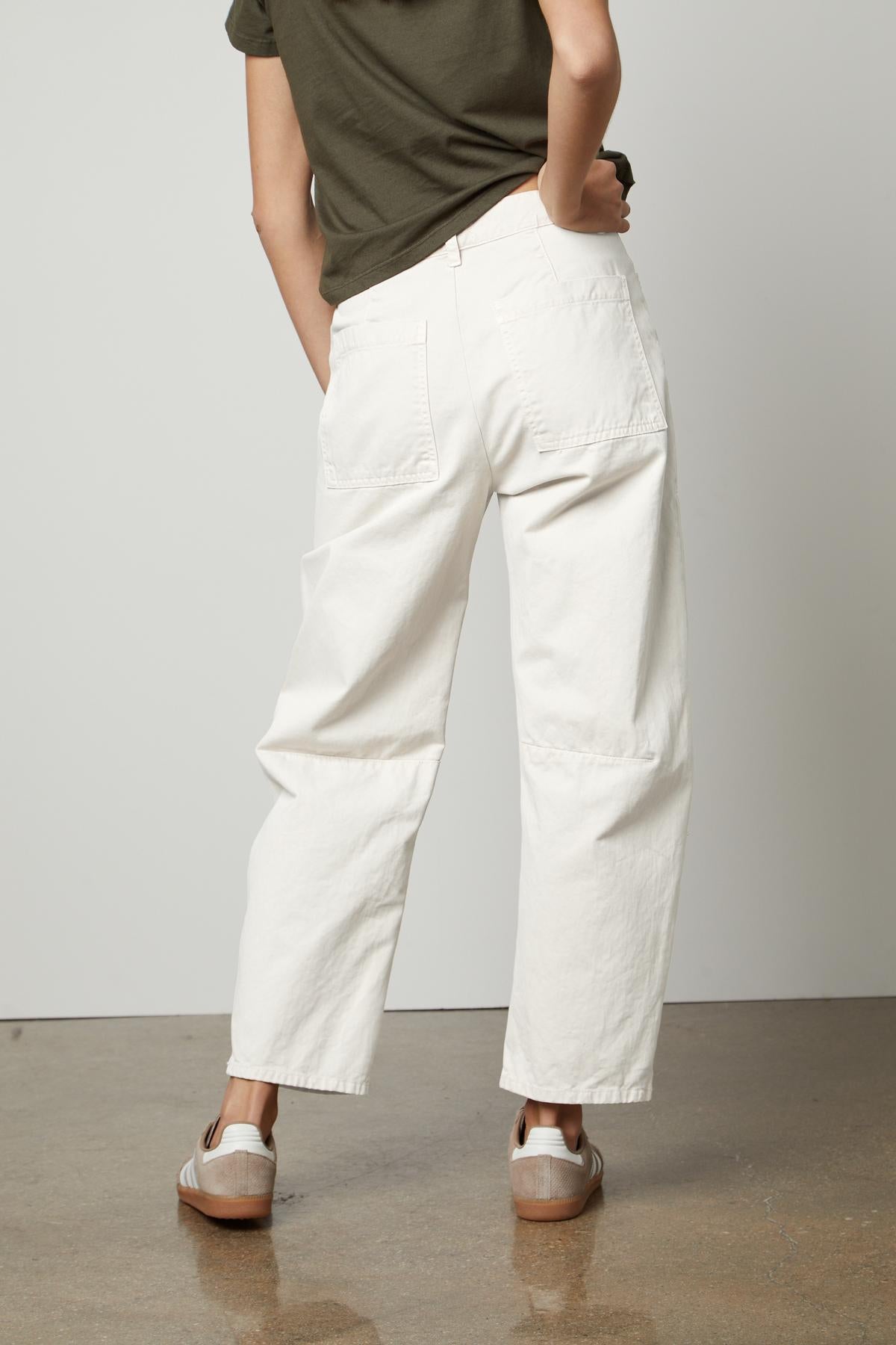 Person wearing Velvet by Graham & Spencer BRYLIE SANDED TWILL UTILITY PANT trouser and brown clogs standing with hands in back patch pockets against a neutral background.