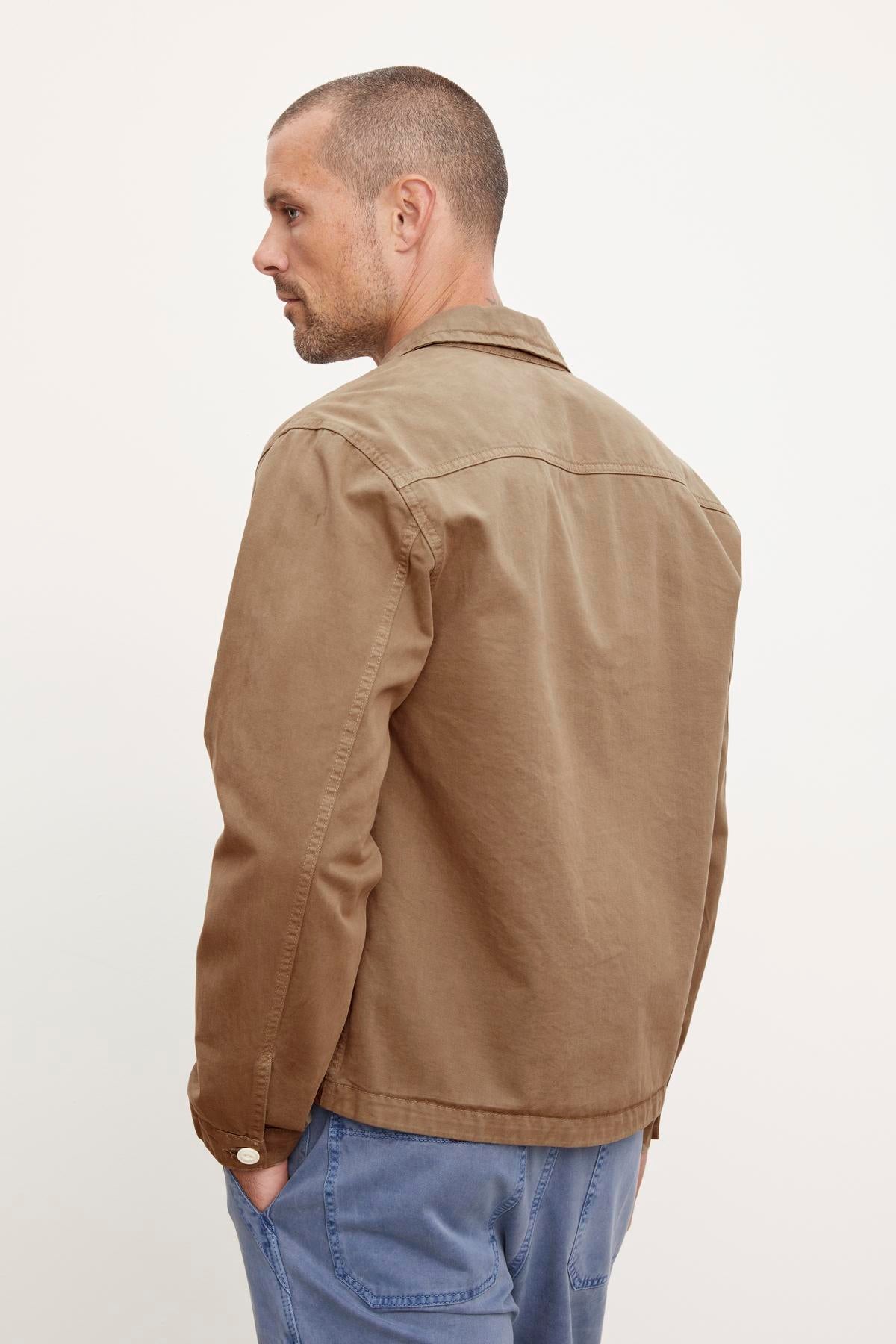 A man in profile wearing a Velvet by Graham & Spencer Flannery Sanded Twill Button-Up Jacket and blue jeans against a neutral background.-36388077699265