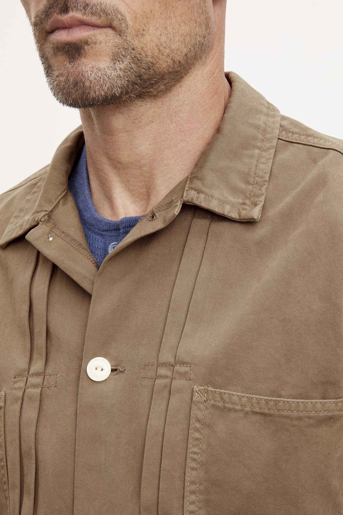 Close-up of a man wearing a FLANNERY SANDED TWILL BUTTON-UP JACKET by Velvet by Graham & Spencer over a blue shirt, exuding a vintage vibe.-36388077732033