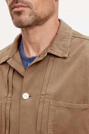 Close-up of a man wearing a FLANNERY SANDED TWILL BUTTON-UP JACKET by Velvet by Graham & Spencer over a blue shirt, exuding a vintage vibe.