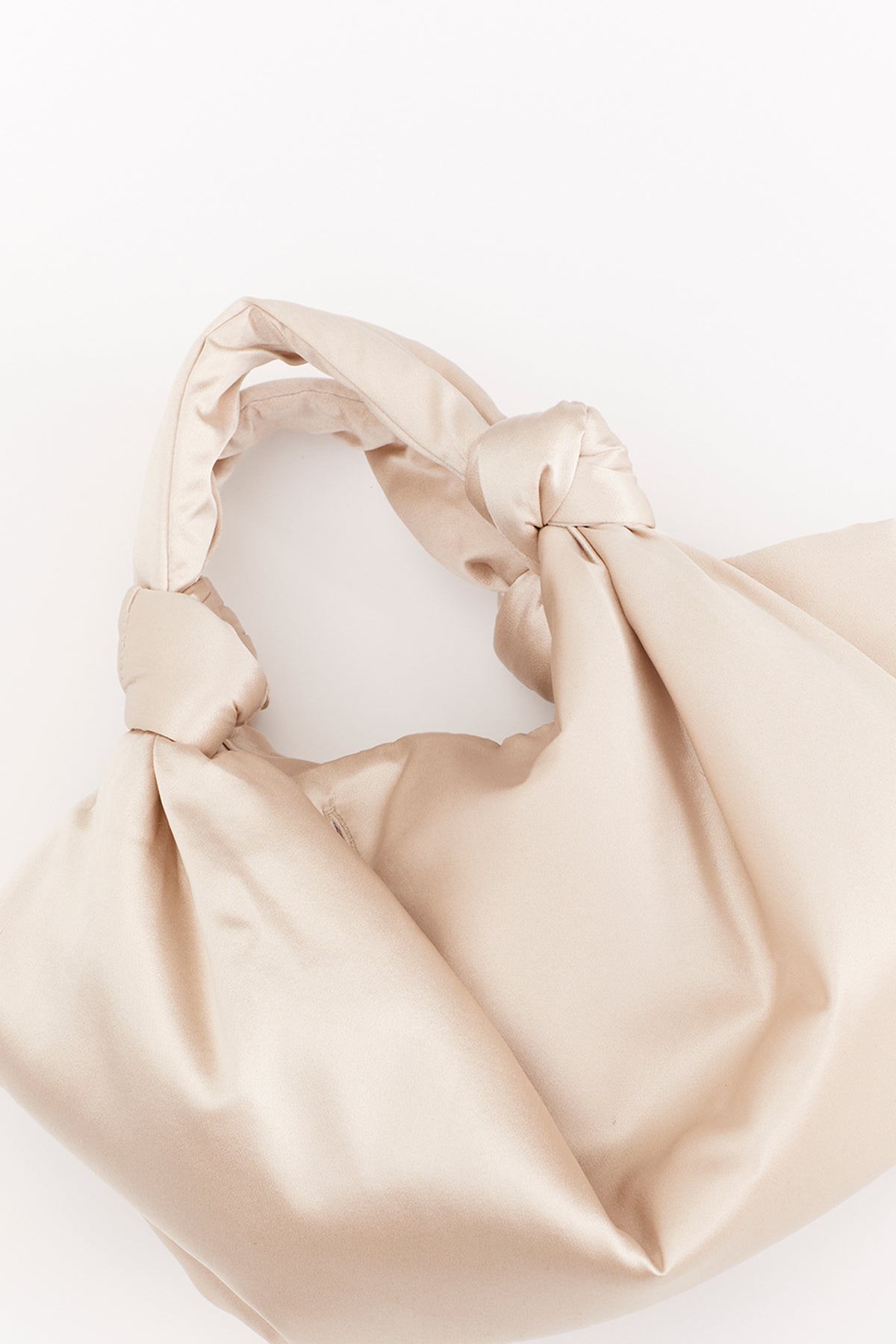 The ROBYN BAG by Velvet by Jenny Graham is a compact beige satin handbag with elegant knot details on the handle, shown against a white background.-39301450629313