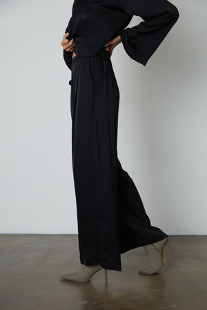 The model is wearing Velvet by Graham & Spencer's LIVI SATIN VISCOSE WIDE LEG PANT with slash pockets and an elastic waistline.