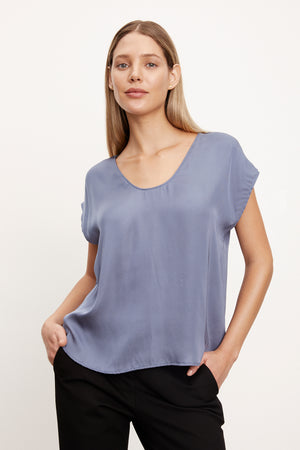 The model is wearing a Velvet by Graham & Spencer KALI SATIN SCOOP NECK TOP in blue.