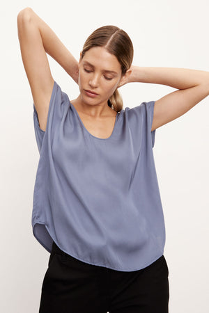 Woman in a luxurious Velvet by Graham & Spencer KALI SATIN SCOOP NECK TOP blouse and black trousers with her hands up, holding her hair.