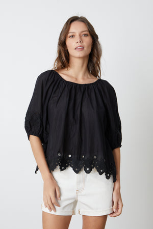 A model wearing a black Velvet by Graham & Spencer ABIGAIL SCHIFFLI EYELET BLOUSE and white shorts.