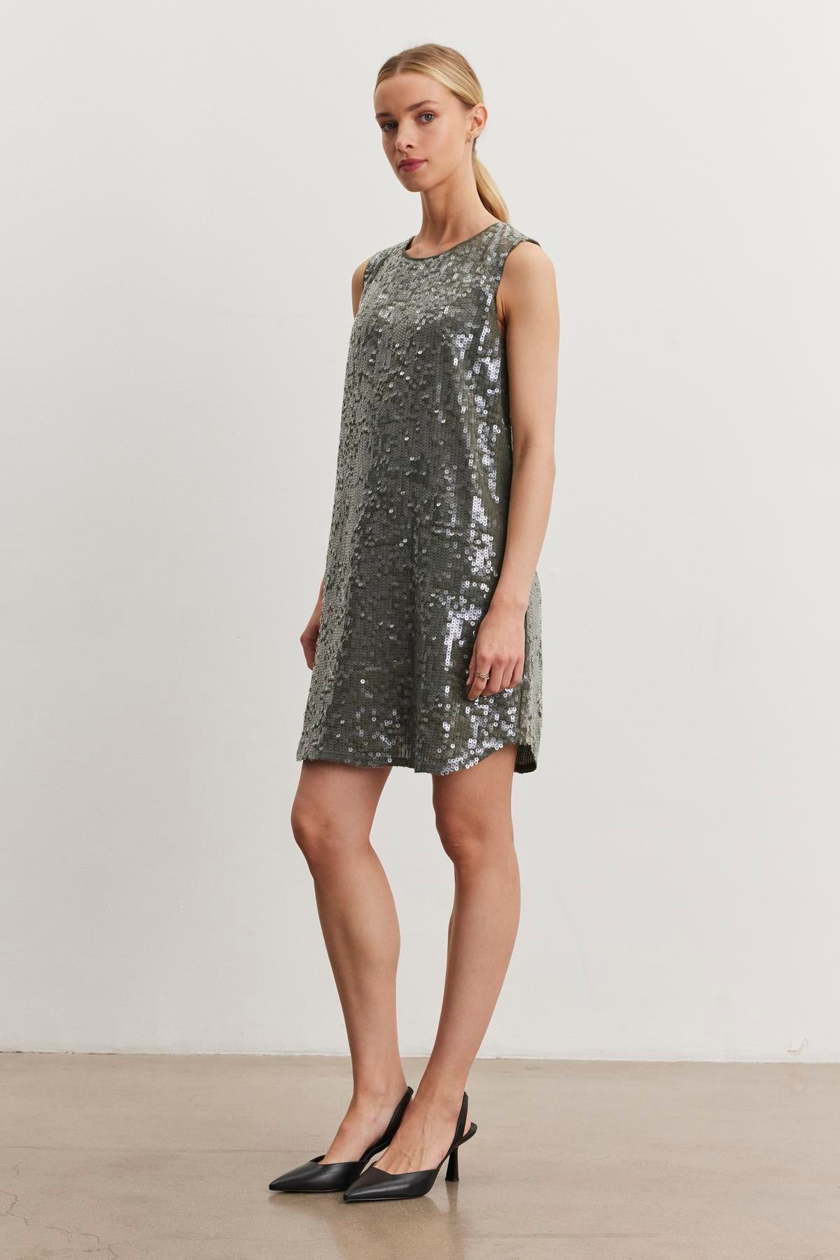 A person stands against a plain white background, wearing the KATHERINE SEQUIN DRESS by Velvet by Graham & Spencer and black heels.-38246520717505