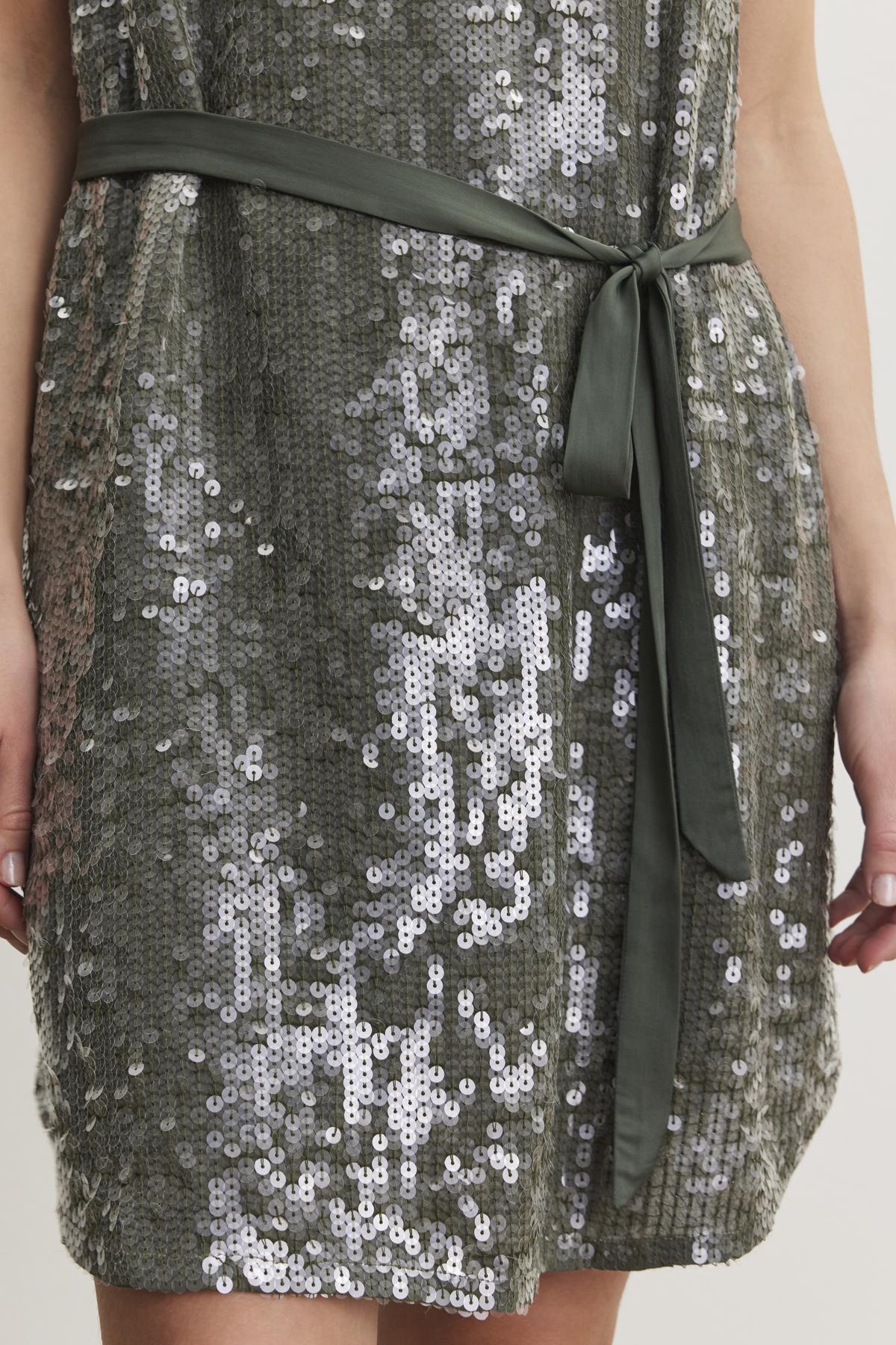 Close-up of the KATHERINE SEQUIN DRESS by Velvet by Graham & Spencer, featuring green sequins and a matching satin belt tied at the waist, worn by a person with hands visible at the sides.-38246520815809