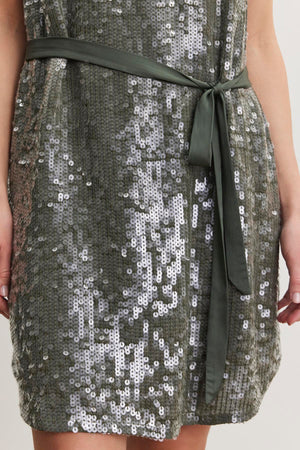 Close-up of the KATHERINE SEQUIN DRESS by Velvet by Graham & Spencer, featuring green sequins and a matching satin belt tied at the waist, worn by a person with hands visible at the sides.