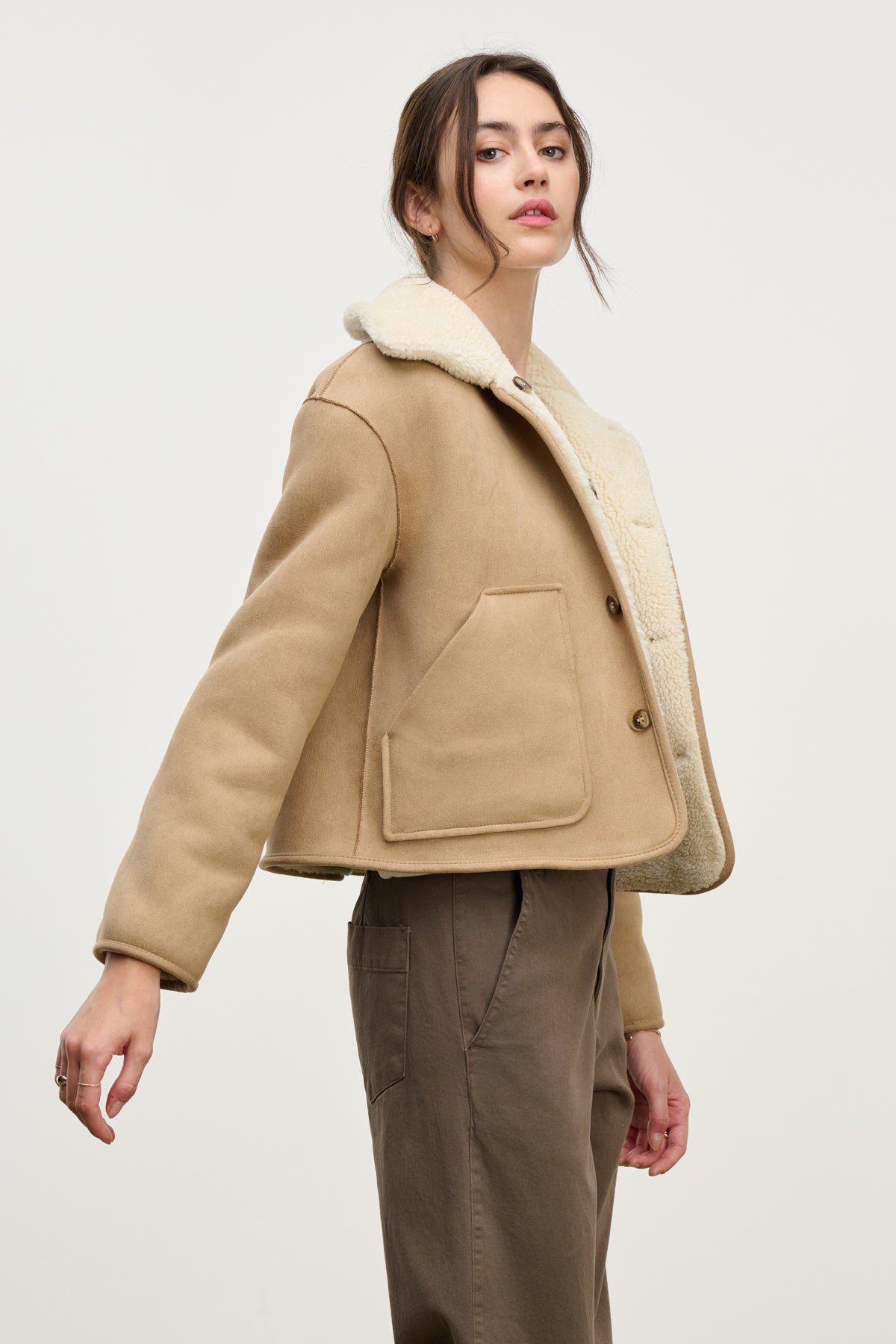 A woman wears the AMARA SHERPA REVERSIBLE JACKET by Velvet by Graham & Spencer, paired with brown pants. She stands against a light background, glancing over her shoulder.-39814804504769