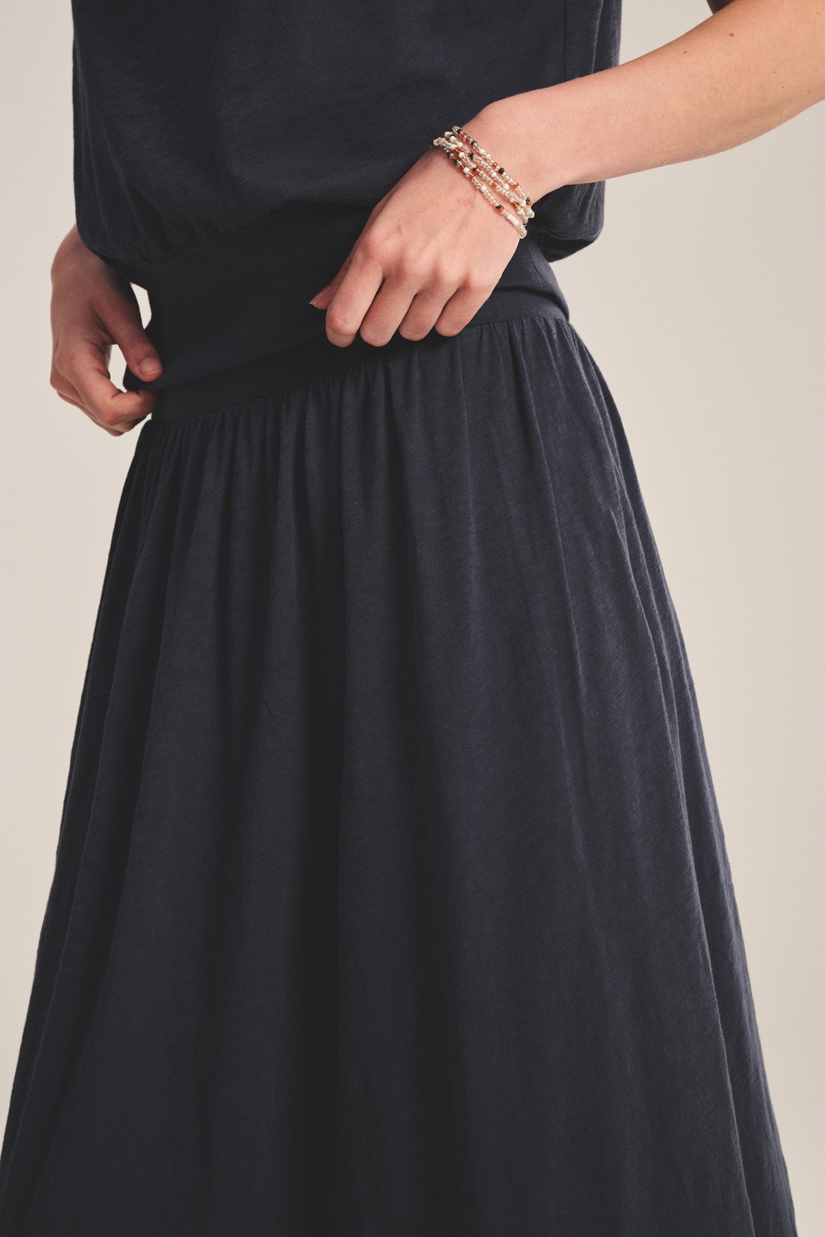 A person wearing the SHILOH SKIRT by Velvet by Graham & Spencer, styled with a relaxed top, one hand on the waistband and the other decorated with beaded bracelets.-41296999153857