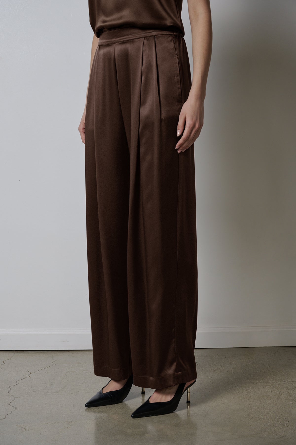 The model is wearing a brown silk jumpsuit with wider leg pants in Velvet by Jenny Graham's MANHATTAN PANT.-36594676629697