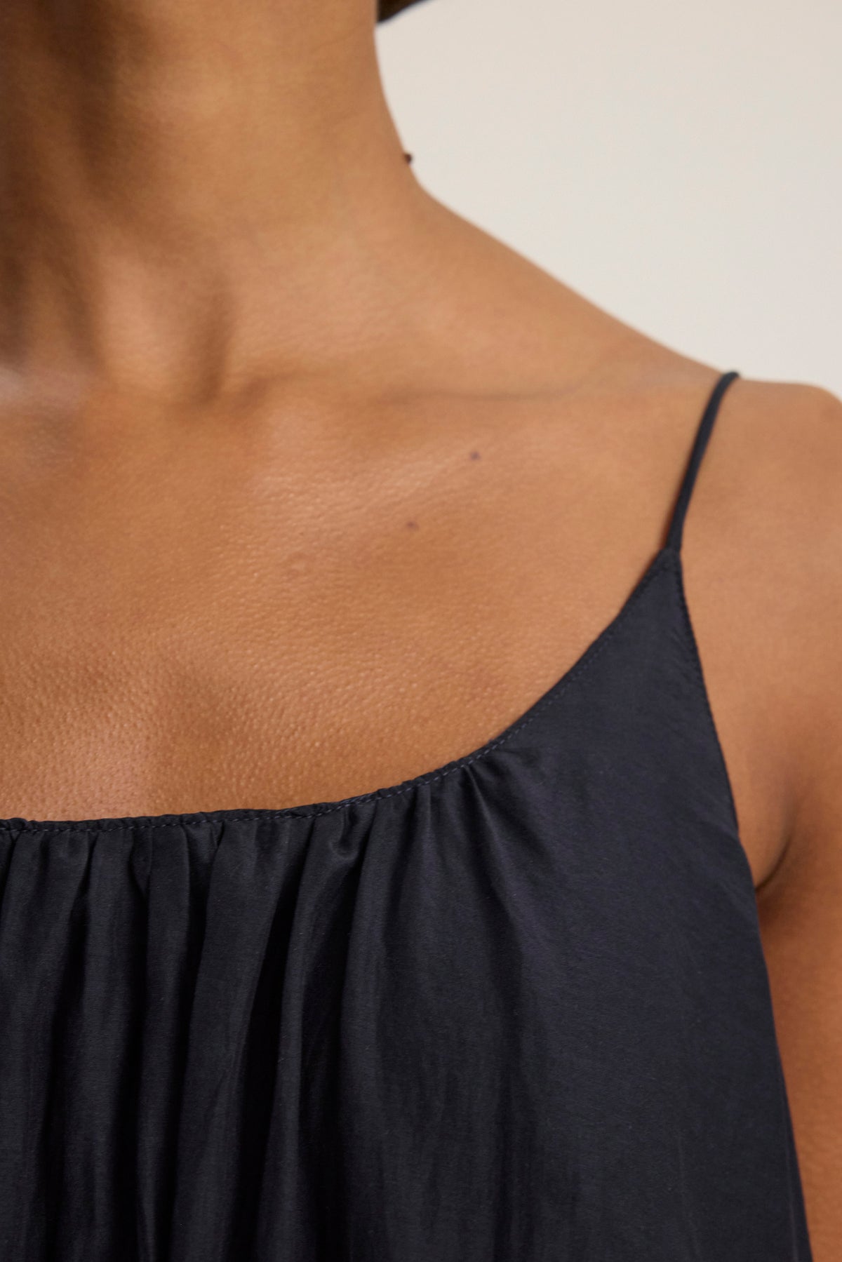 Close-up of a person's upper chest and shoulder wearing the AVERY SILK COTTON VOILE DRESS by Velvet by Graham & Spencer, featuring black spaghetti straps and a scoop neckline against a neutral background.-39123371786433