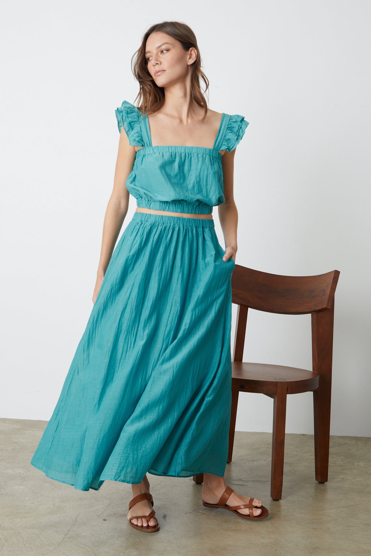 A woman in the MARIELA MAXI SKIRT by Velvet by Graham & Spencer standing next to a chair.