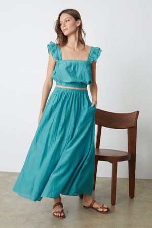 A woman in the MARIELA MAXI SKIRT by Velvet by Graham & Spencer standing next to a chair.