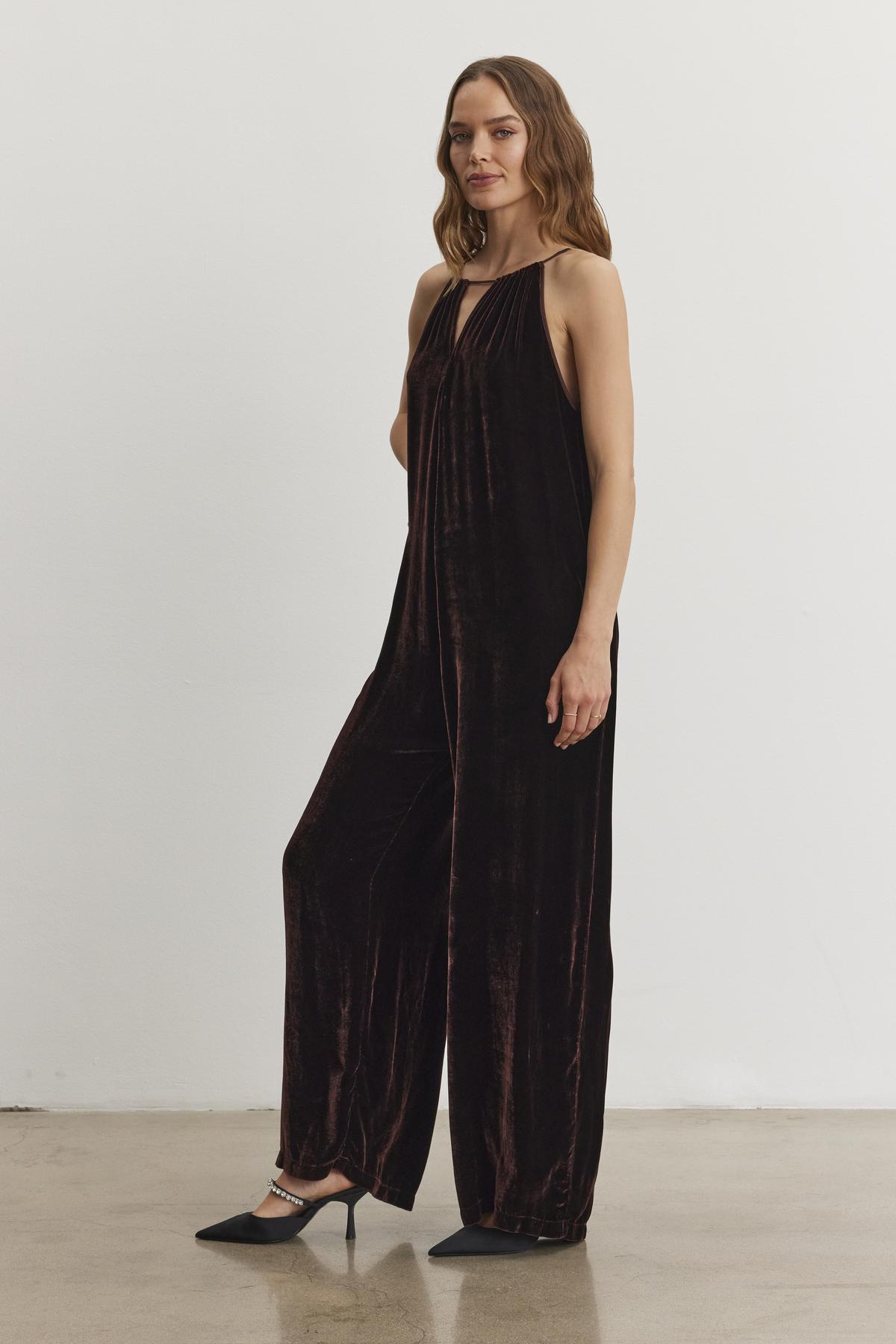 A woman in the CIENNA Silk Velvet Jumpsuit by Velvet by Graham & Spencer is standing with one arm relaxed, wearing black shoes against a plain white background.-38246397313217