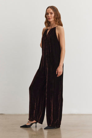 A woman in the CIENNA Silk Velvet Jumpsuit by Velvet by Graham & Spencer is standing with one arm relaxed, wearing black shoes against a plain white background.
