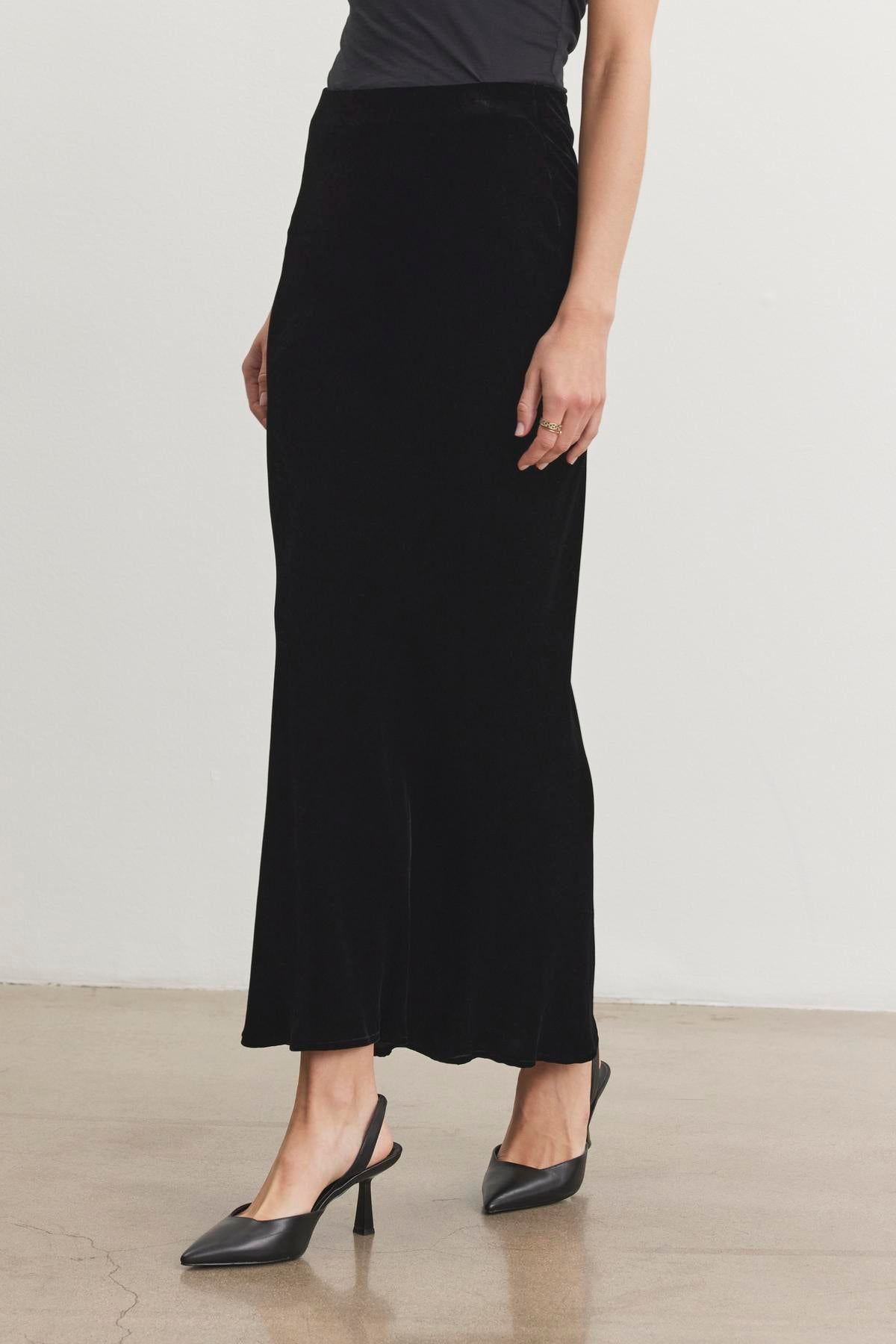 An individual is wearing the EZA SILK VELVET SKIRT by Velvet by Graham & Spencer along with black heels while standing on a polished floor.