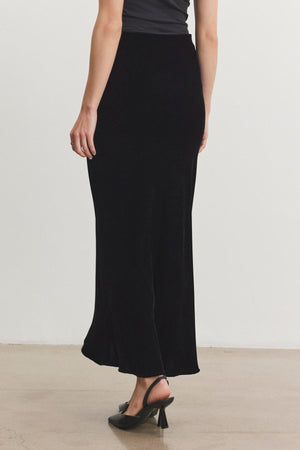 A person wearing the EZA Silk Velvet Skirt by Velvet by Graham & Spencer and a black top stands on a light-colored floor, facing away. They complete the look with black heels.